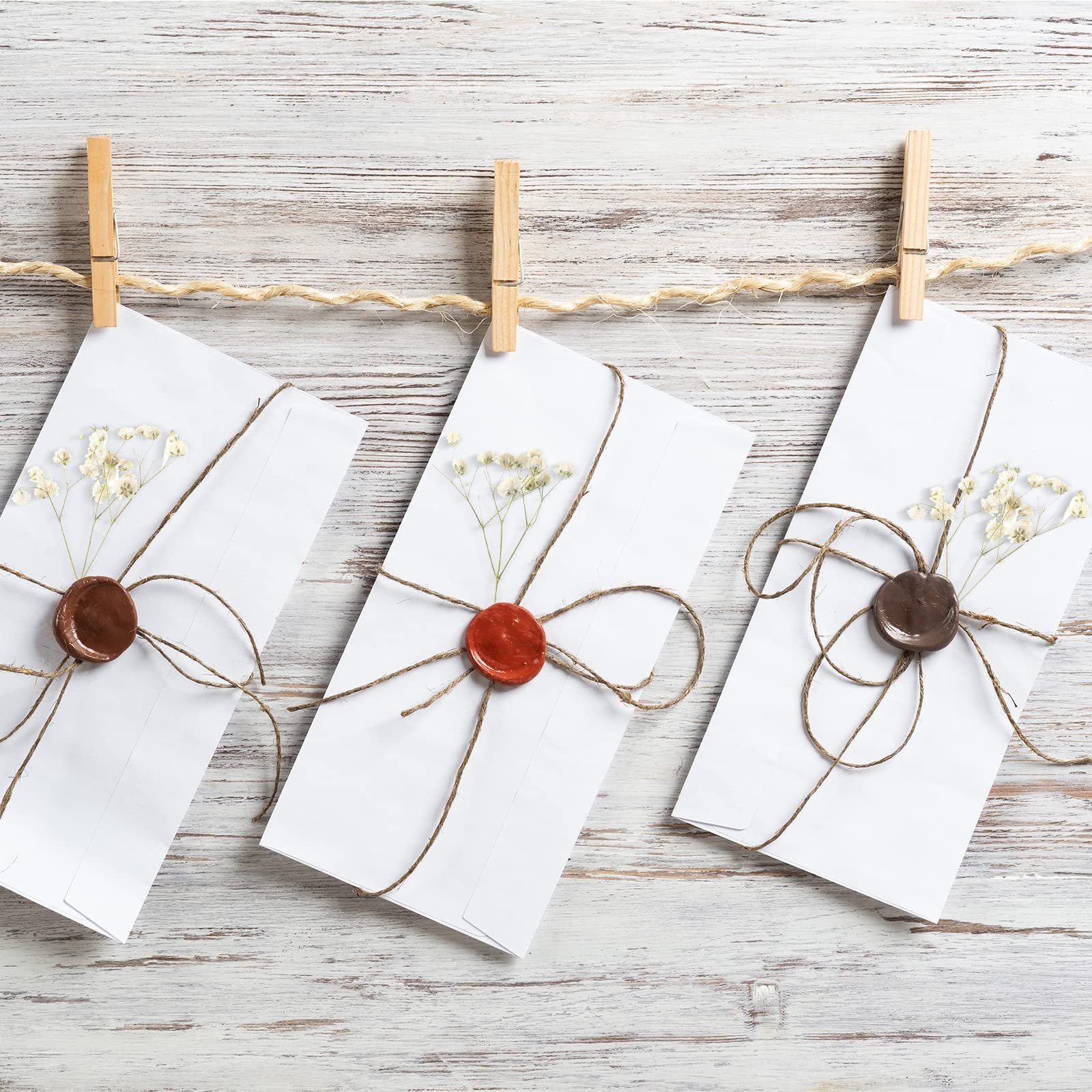 Three white envelopes with dried baby's breath and wax seals hanging on a twine clothesline