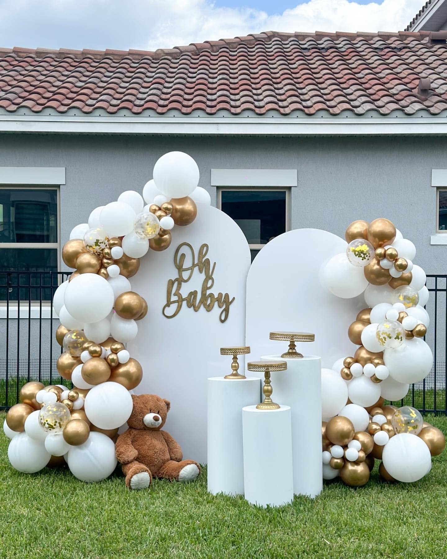 White and gold balloon arch with 'Oh Baby' sign and teddy bear for a baby shower setup