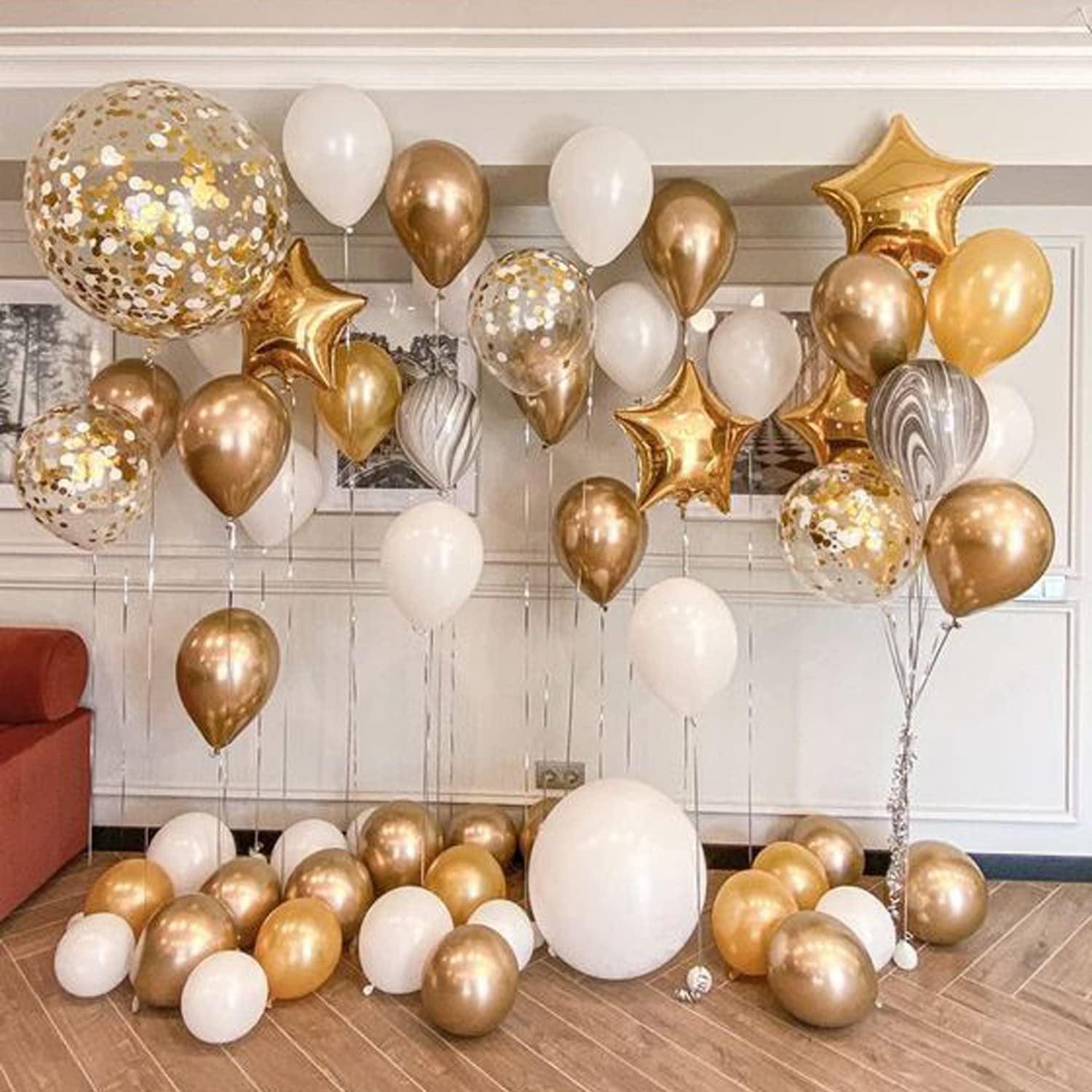 Assortment of white, gold, and confetti balloons arranged on a wooden floor and against a wall.