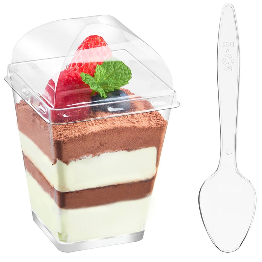 Clear plastic dessert cup with lid filled with layered mousse and topped with berries and mint, next to a clear plastic spoon.