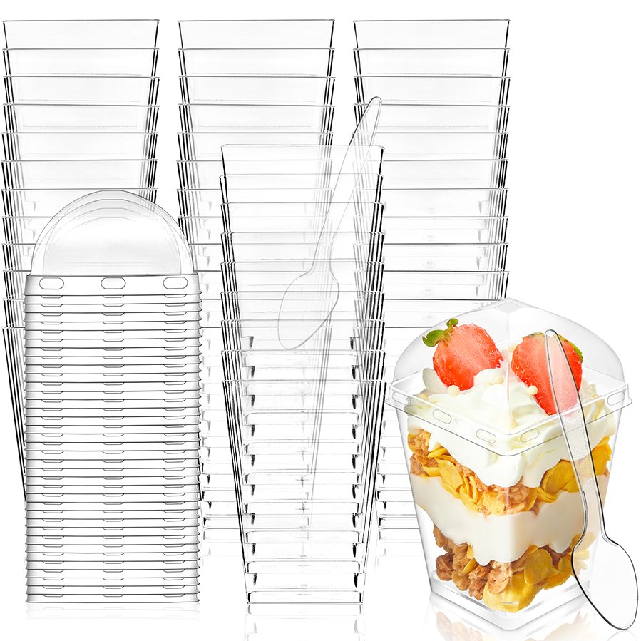 Stack of clear plastic dessert cups with lids and spoons, one cup filled with parfait and topped with strawberries.