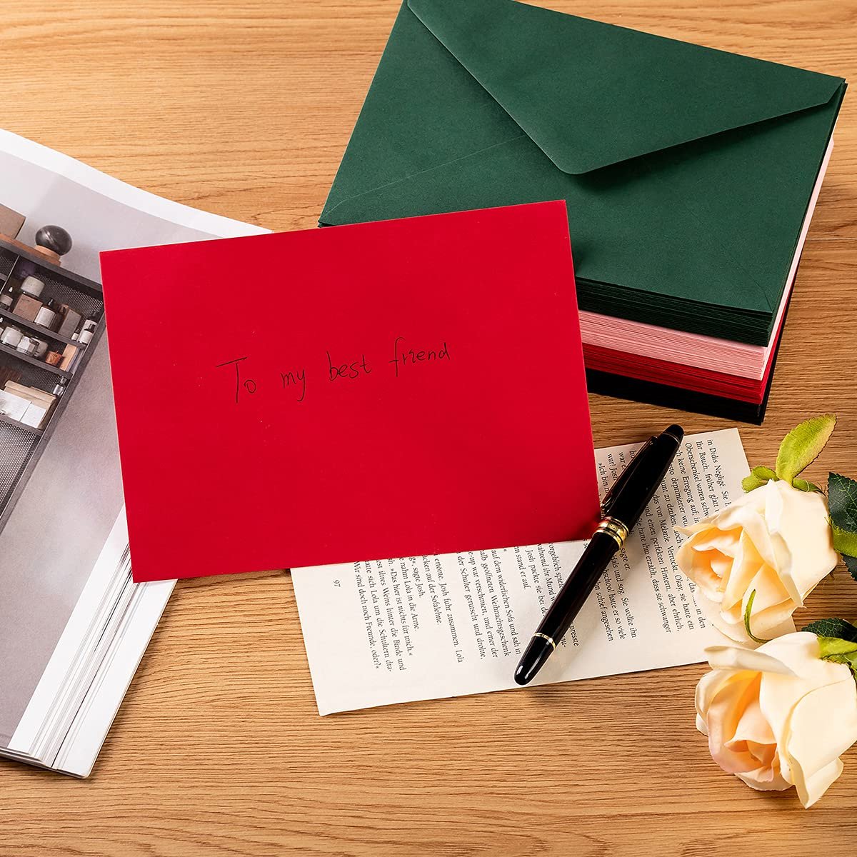 Red envelope with handwritten message 'To my best friend' next to a stack of dark green envelopes and a pen on a wooden surface.
