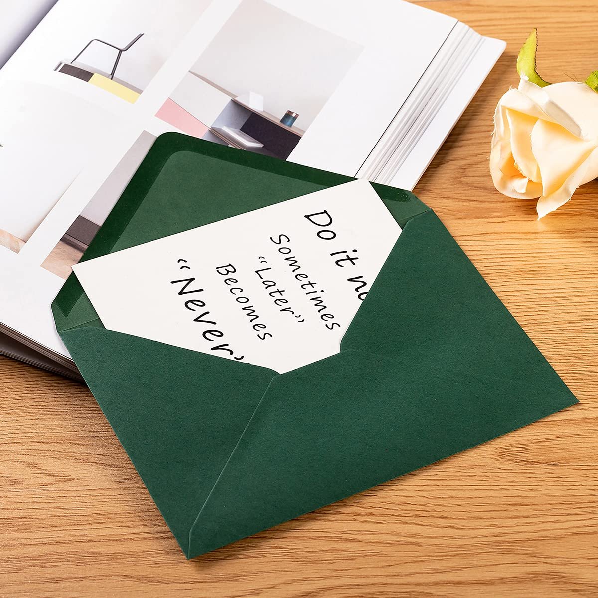 Dark green A7 envelope with a card inside featuring handwritten text on a wooden desk with a book and rose.