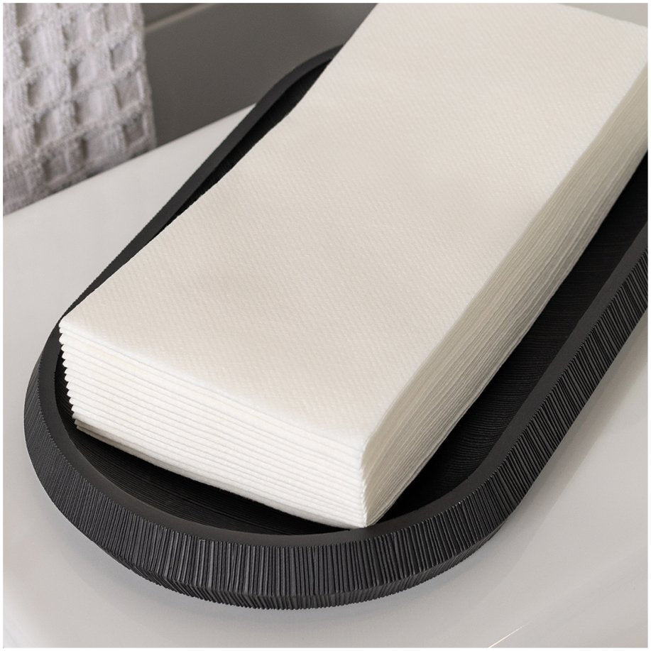 Stack of white linen-feel paper guest towels in a black oval tray on a countertop.