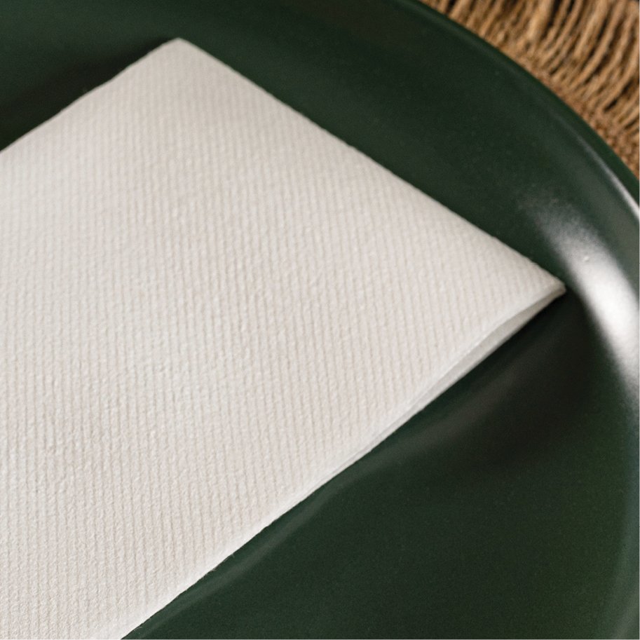 White linen-feel paper guest towel folded on a dark green plate with a burlap texture background