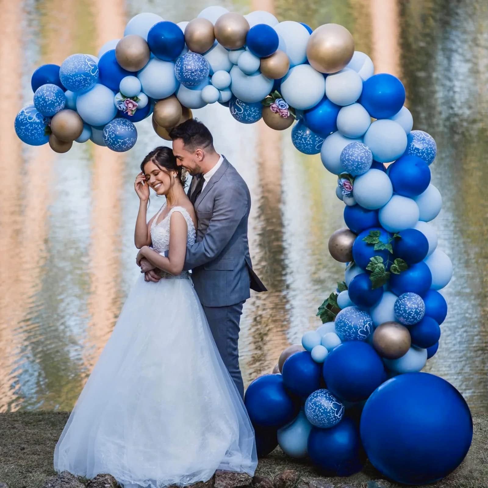 Bride and groom embracing under a balloon arch with royal blue, light blue, and gold balloons.