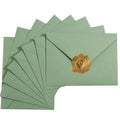 Sage-green A7 envelopes fanned out with a gold heart-shaped wax seal sticker on one envelope.
