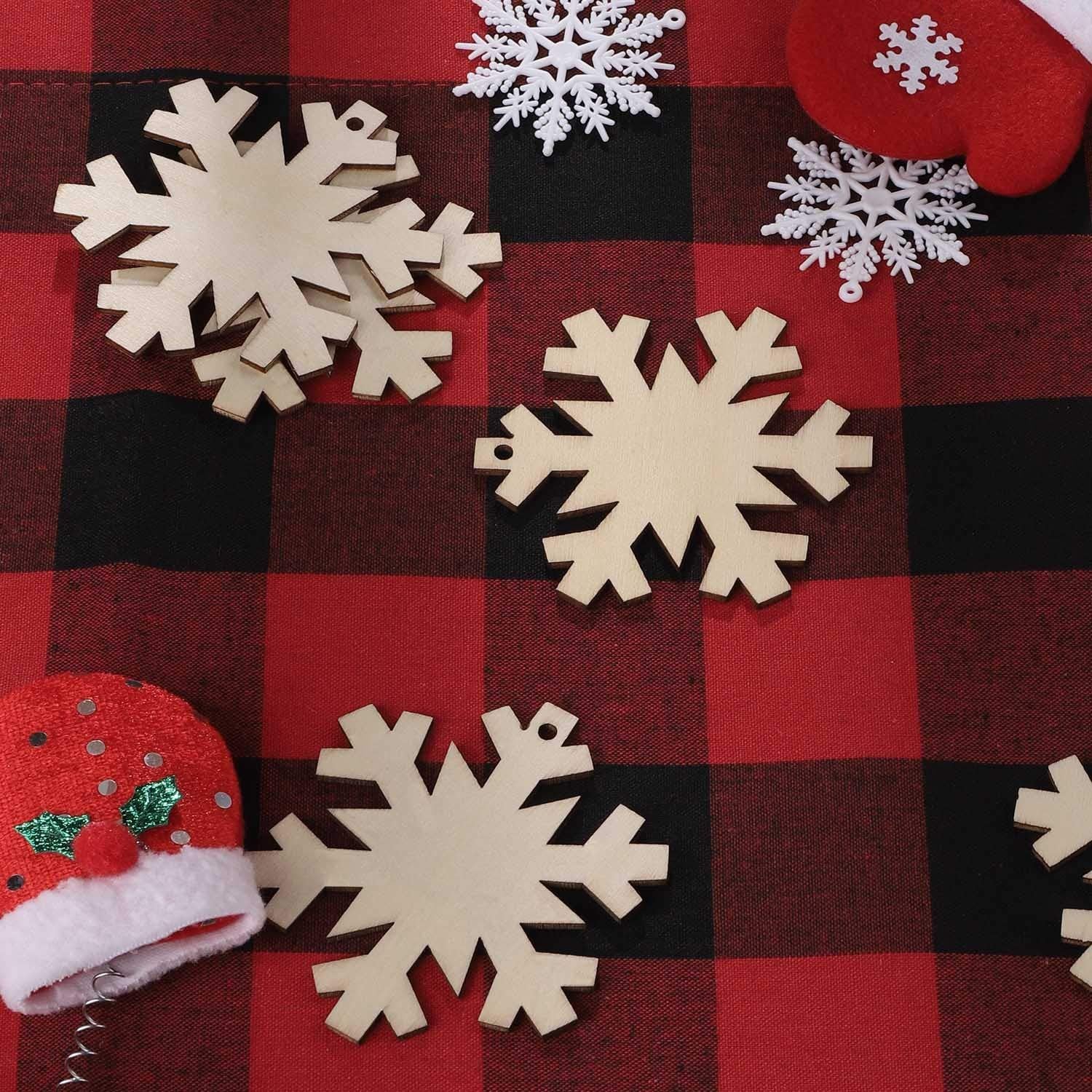 Unfinished wooden snowflake ornaments scattered on a red and black buffalo plaid background with decorative Christmas elements.