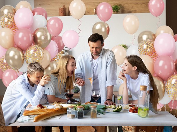 Family celebrating around a table with pink and gold balloons overhead
