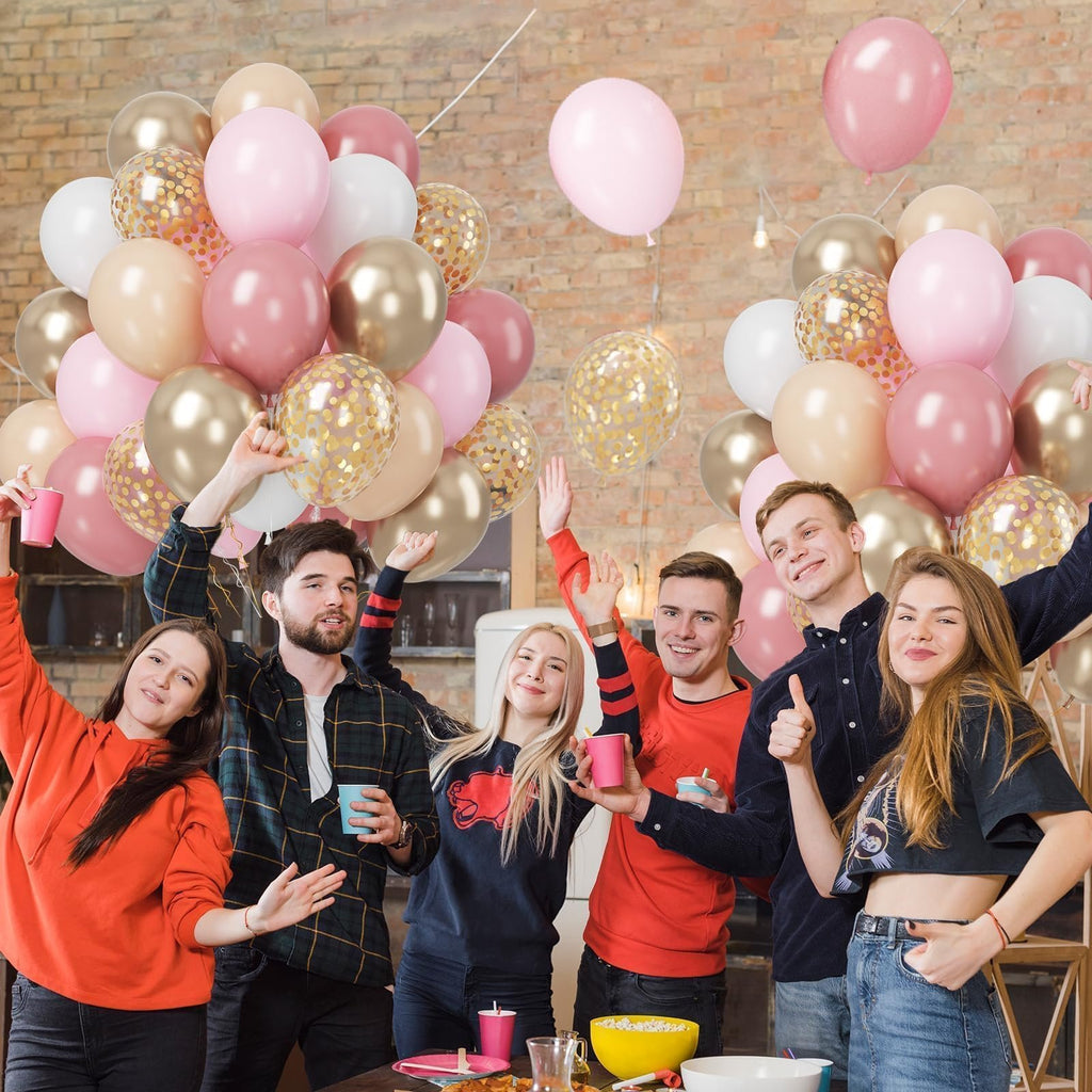 Group of young adults celebrating with pink, gold, and confetti balloons at a party.