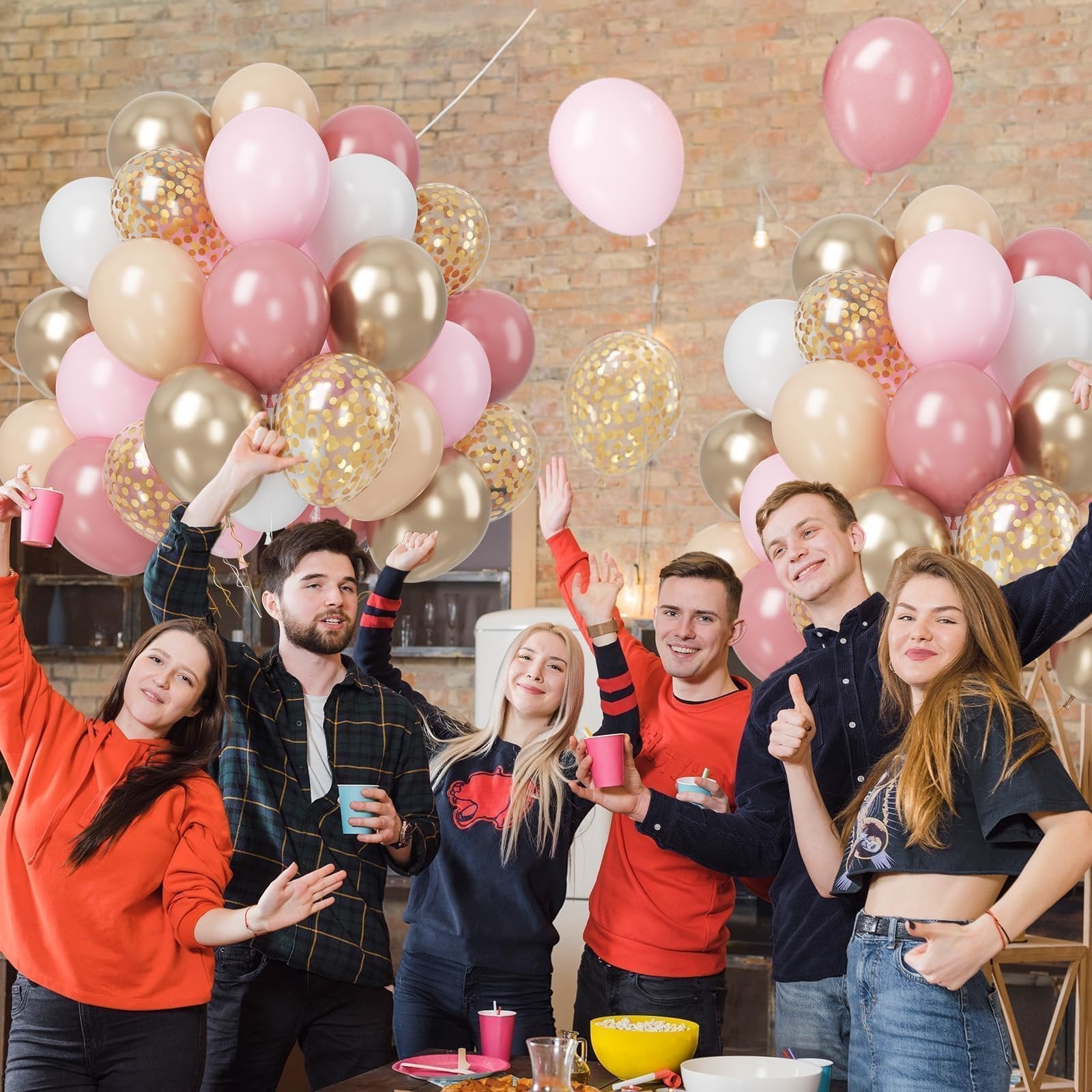 Group of young adults celebrating with pink, gold, and confetti balloons at a party.