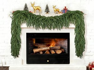 Artificial Norfolk pine garland draped over a fireplace with a lit fire inside.