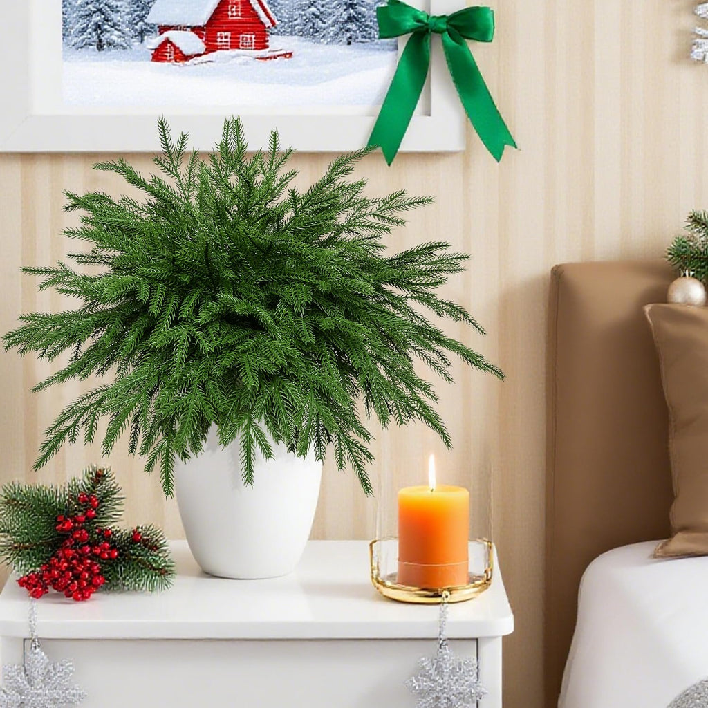Artificial pine stems in a white pot on a nightstand with a lit candle and Christmas decor