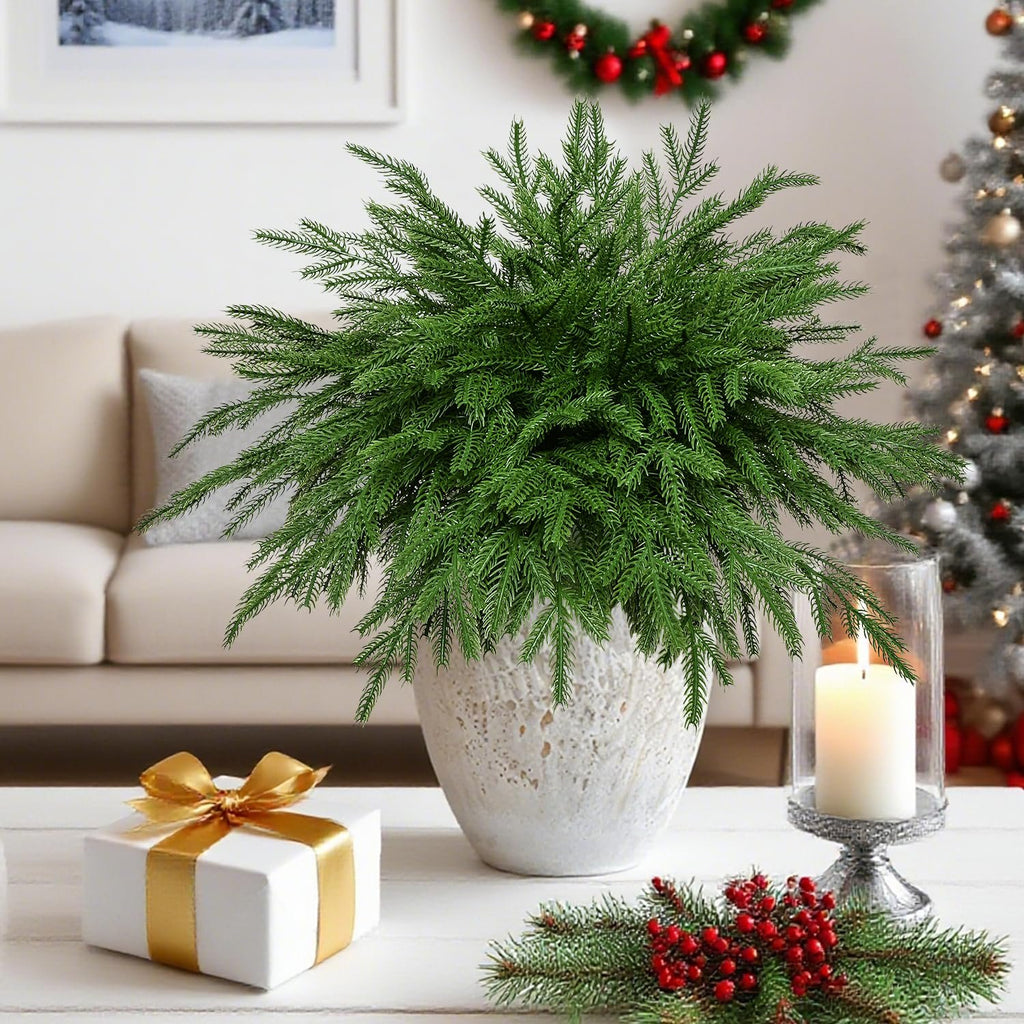 Artificial Norfolk pine stems in a decorative pot on a table with a gift and candle