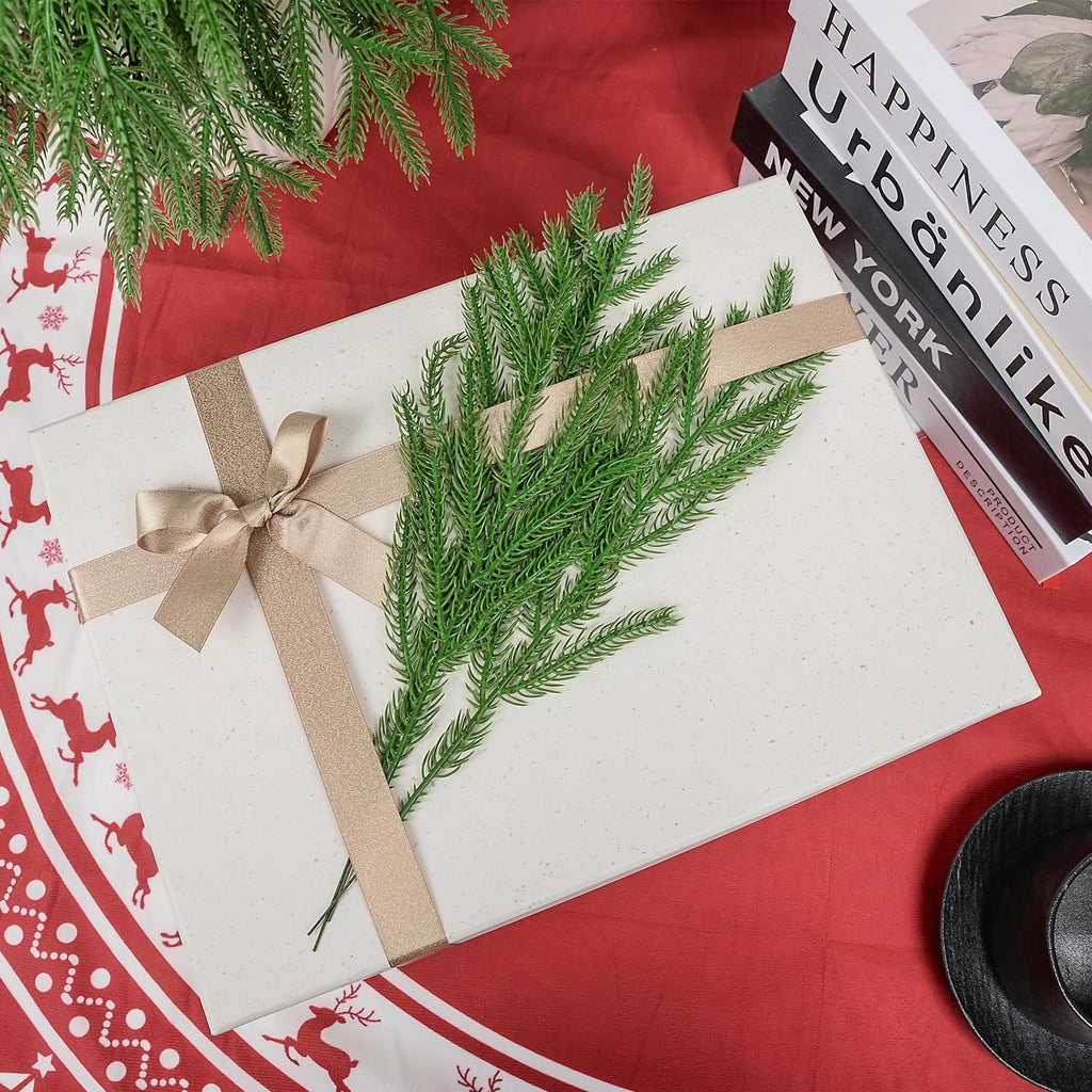 Artificial pine sprigs on a gift box with a gold ribbon, surrounded by holiday decor and books.