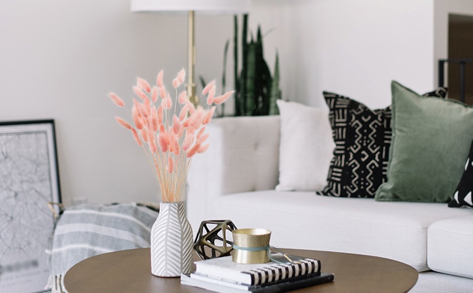 Vase of pink bunny tail grass on a coffee table in a living room setting with a sofa and pillows