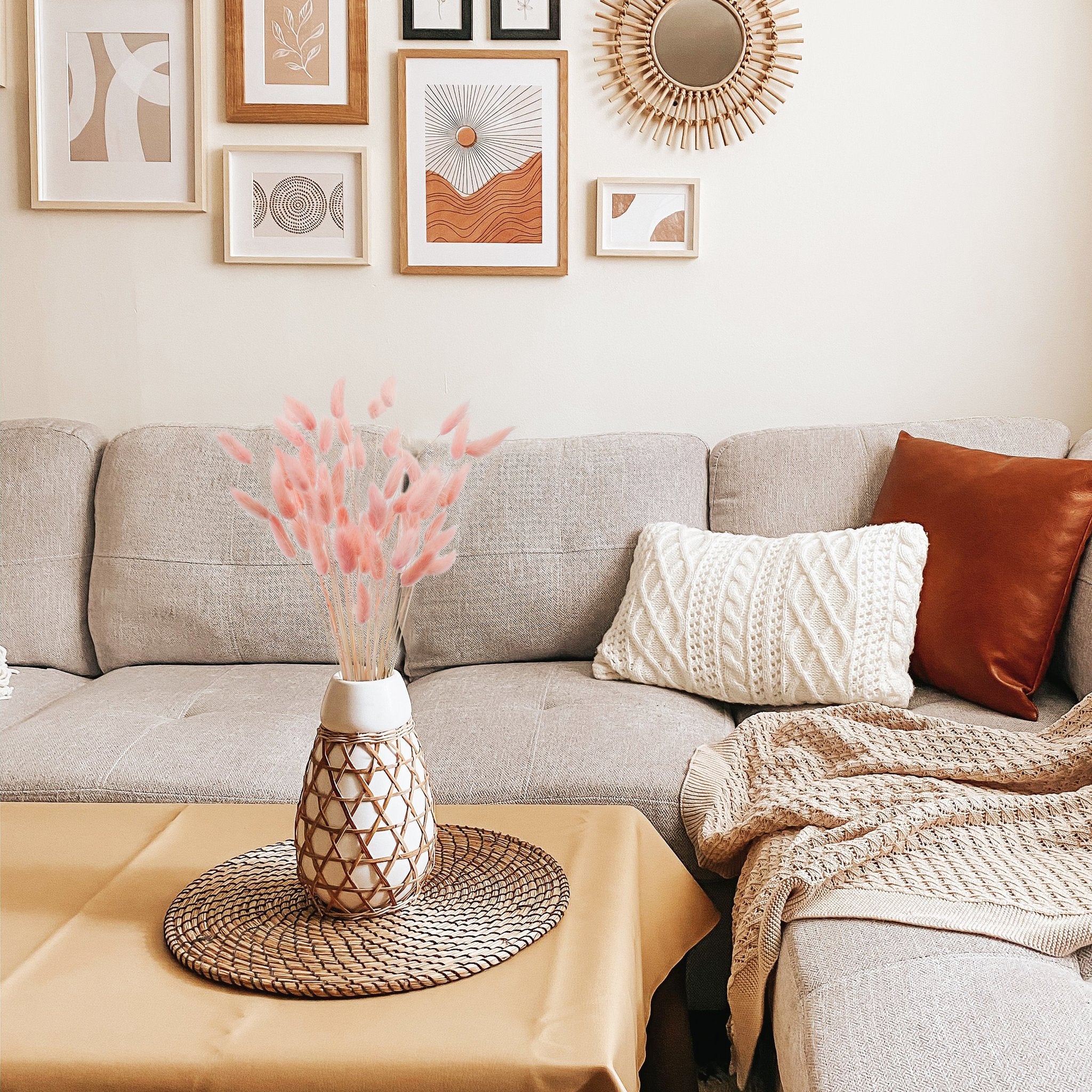 Pink bunny tail grass in a vase on a table in a boho living room setting with framed art and a sofa