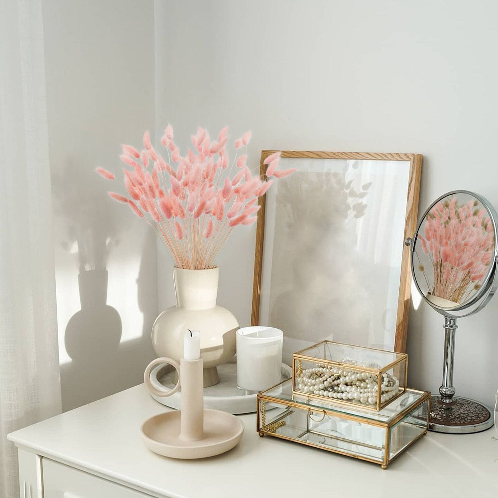 Pink bunny tail grass in a vase on a dresser with decorative items and a mirror reflection