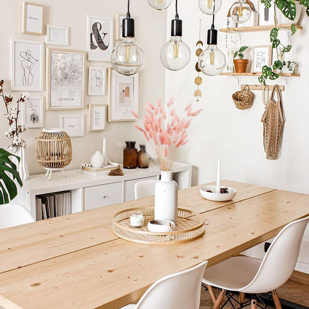 A vase of pink bunny tail grass on a wooden dining table with chairs and wall decor.