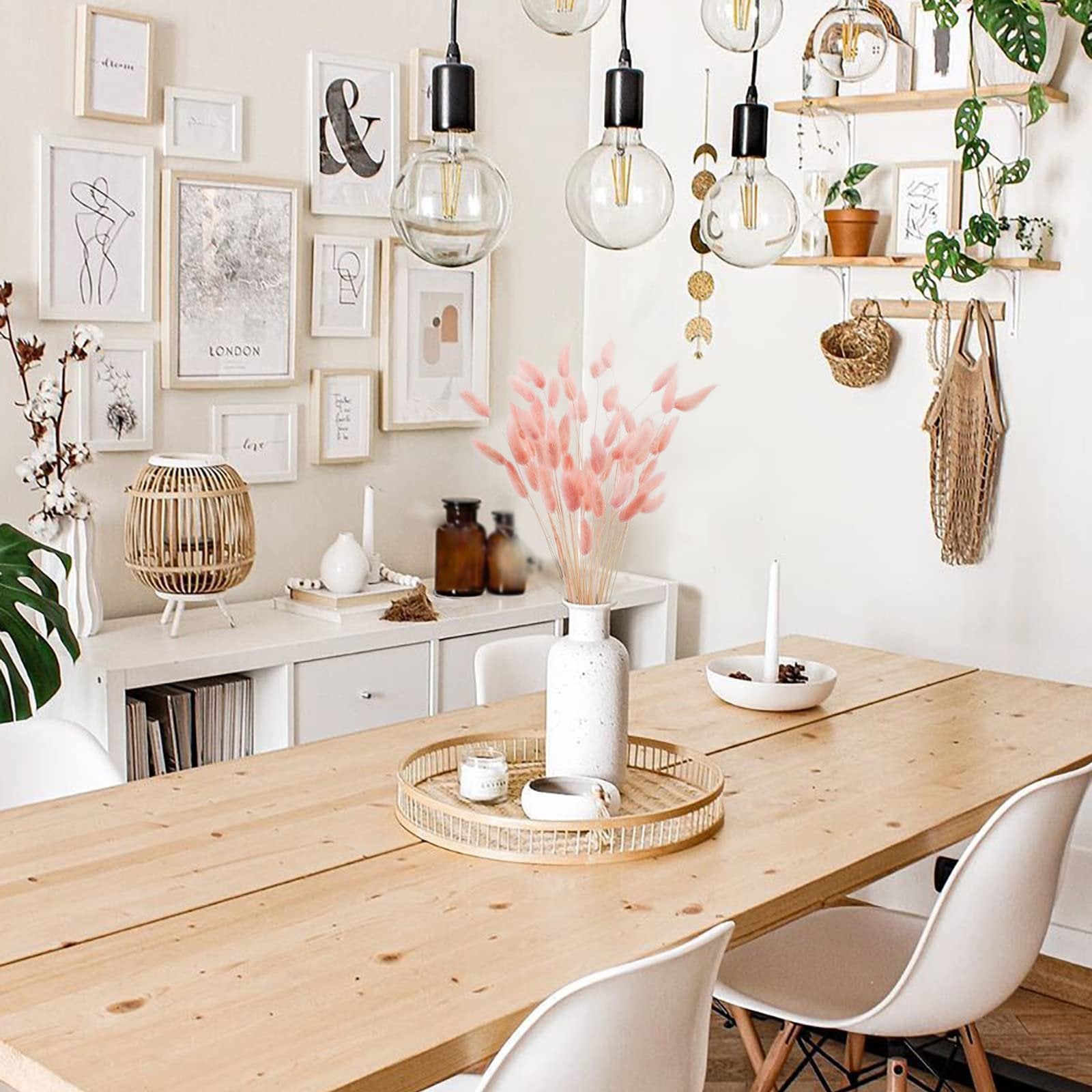 A vase of pink bunny tail grass on a wooden dining table with chairs and wall decor.