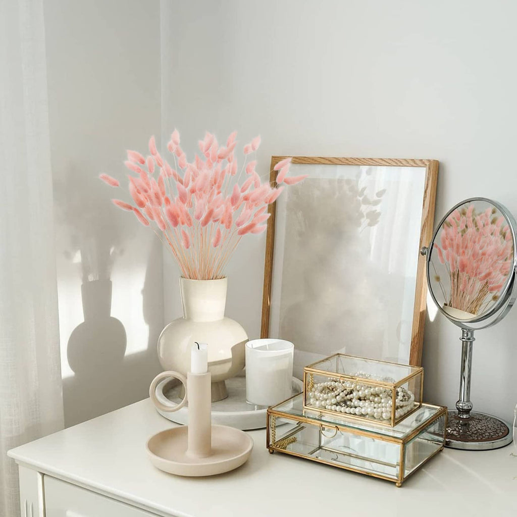 Pink bunny tail grass in a vase on a dresser with decorative items and a mirror