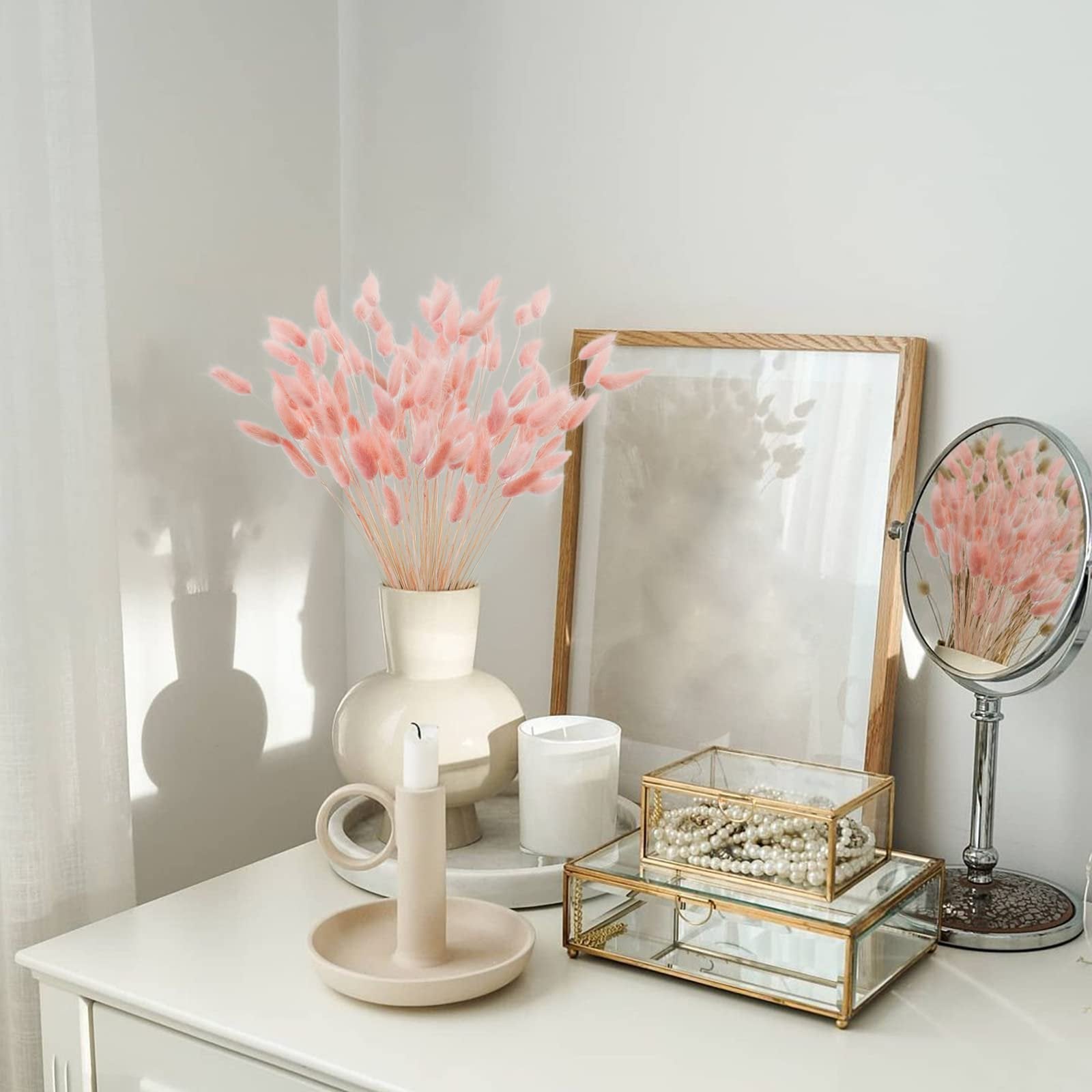 Pink bunny tail grass in a vase on a dresser with decorative items and a mirror