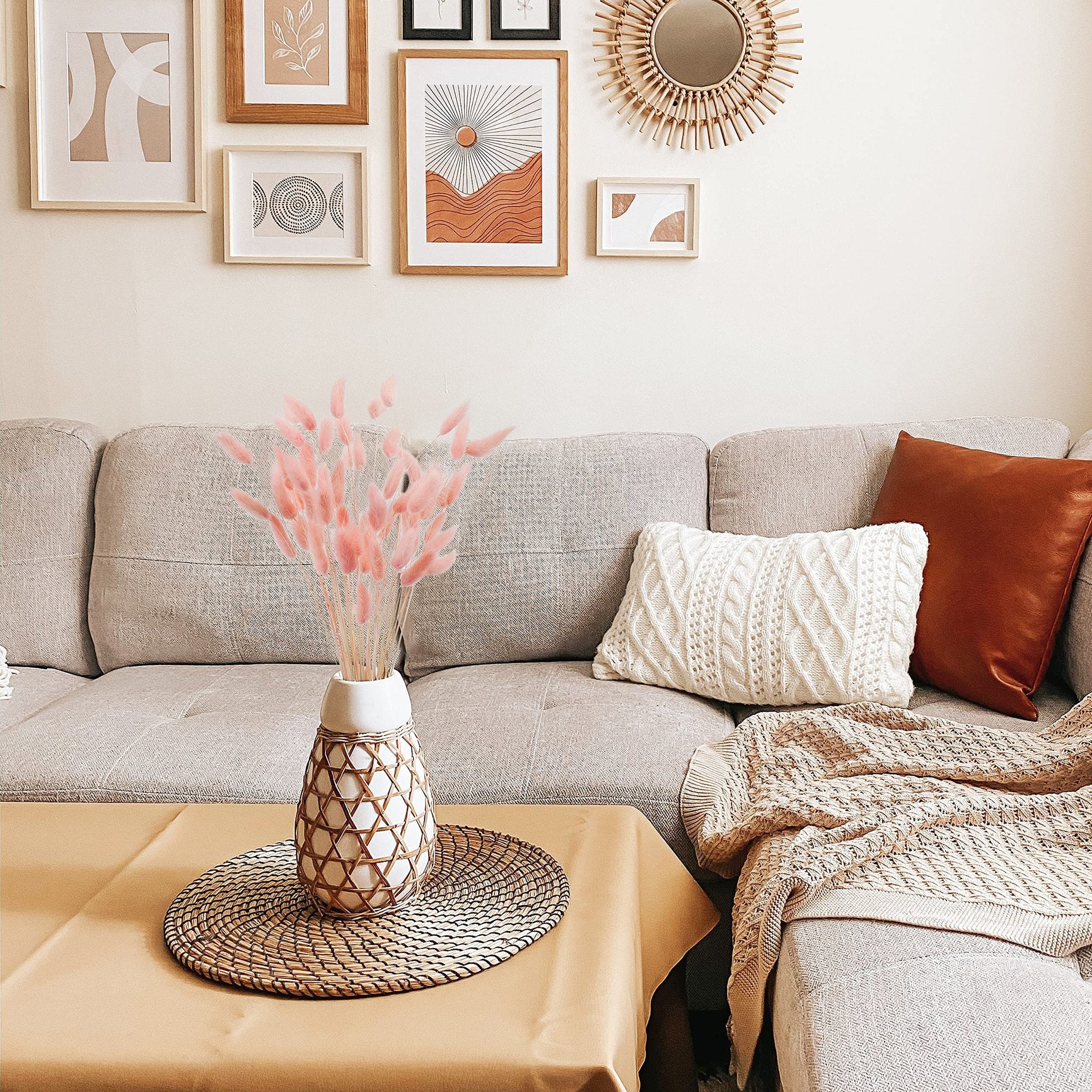 Pink bunny tail grass in a woven vase on a table in front of a sofa with decorative pillows and a blanket.
