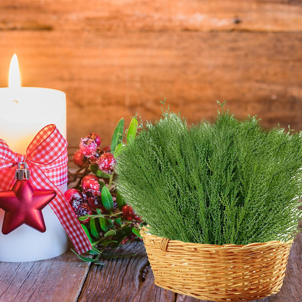 Artificial pine branches in a basket next to a lit candle with a red star ornament and berries