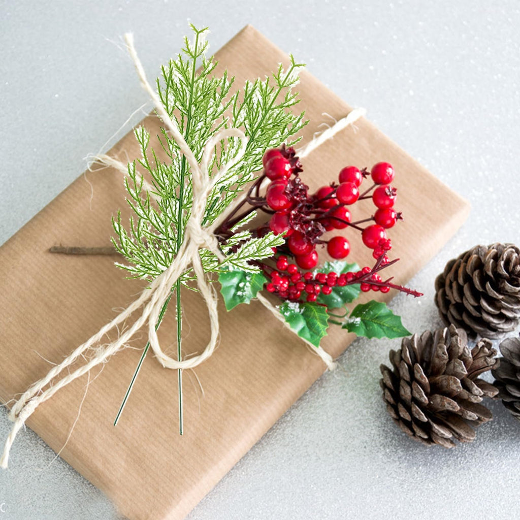 Artificial pine branches and red berries tied with twine to a brown paper wrapped gift, with pine cones on the side.