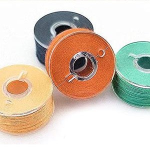 Four sewing machine bobbins with thread, two orange, one teal, and one yellow, arranged on a white surface.