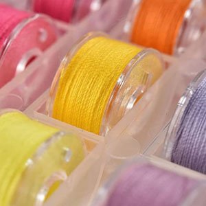 Close-up of colorful sewing machine bobbins filled with thread in a clear plastic organizer case.