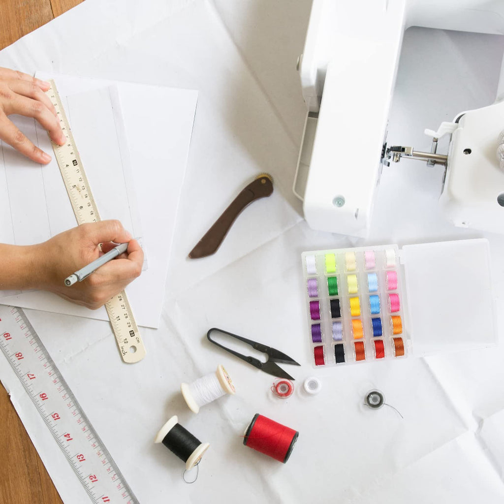 Overhead view of sewing supplies including a sewing machine, colorful bobbins, thread spools, scissors, and rulers on white paper.