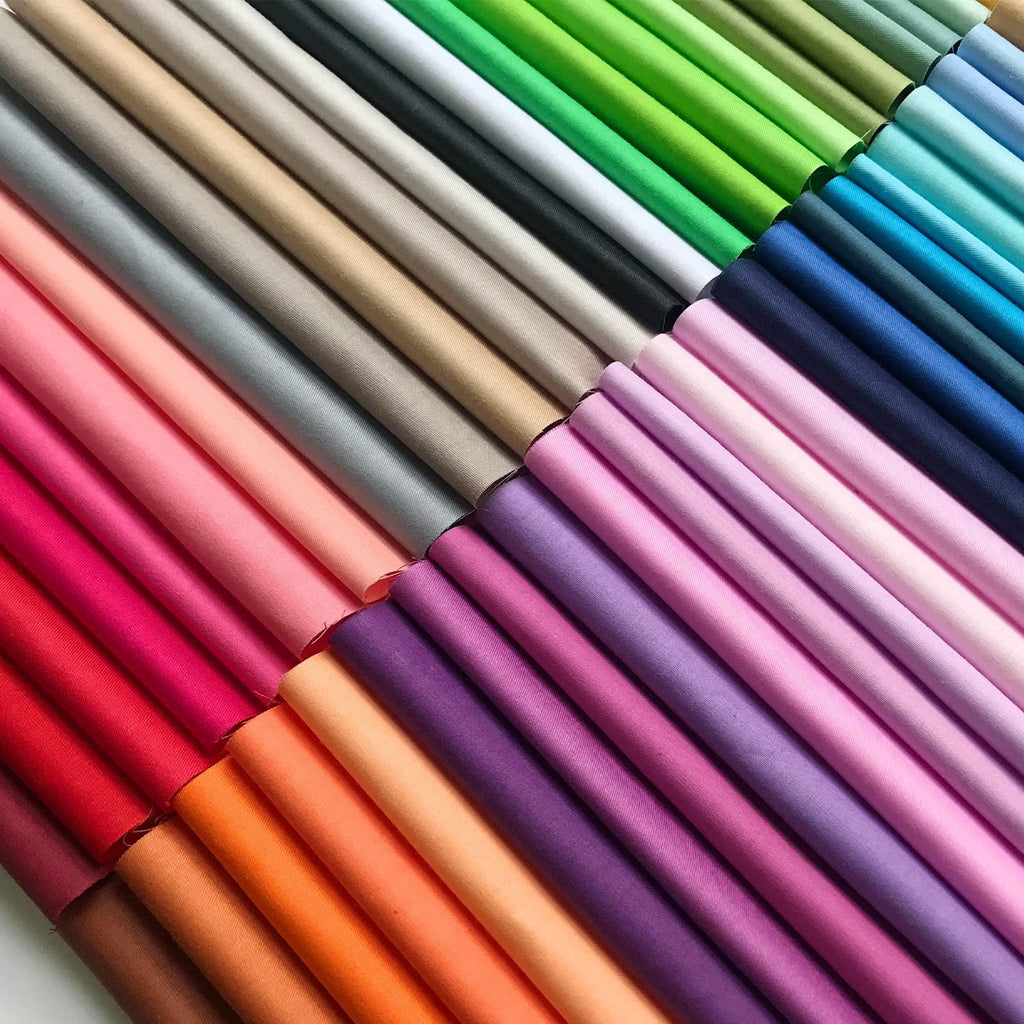 Assortment of 50 solid color 10x10 inch cotton fabric squares, neatly folded and arranged in diagonal rows.