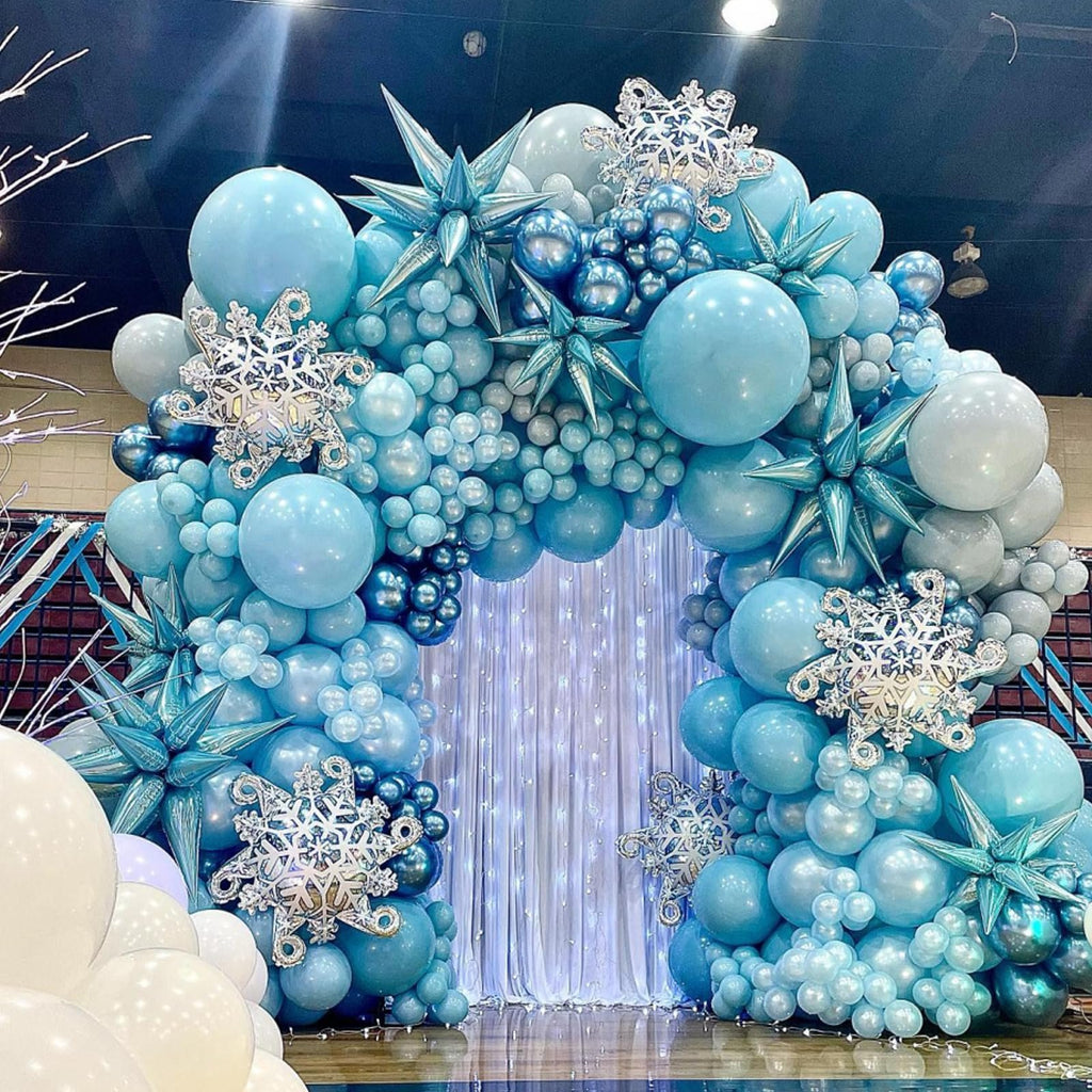 Archway balloon garland in shades of blue and white, decorated with snowflake and starburst accents, set against a sparkly curtain backdrop.