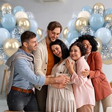 Group of five people embracing, surrounded by dusty blue, gold, and confetti balloons.