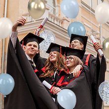 Graduating students in caps and gowns taking a selfie with balloons and diplomas