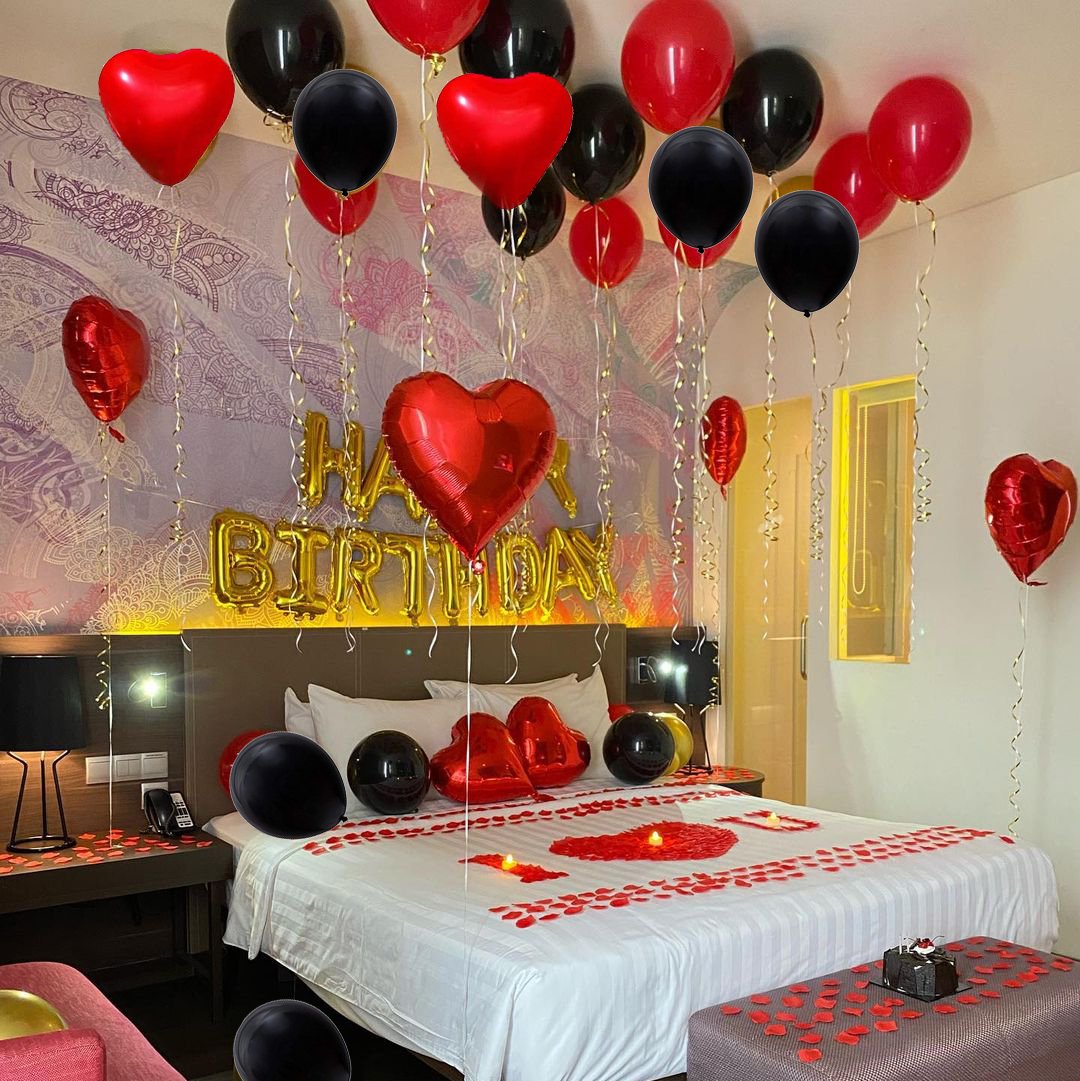 Bedroom decorated for a birthday with red and black balloons, heart shapes, and 'Happy Birthday' foil banner.