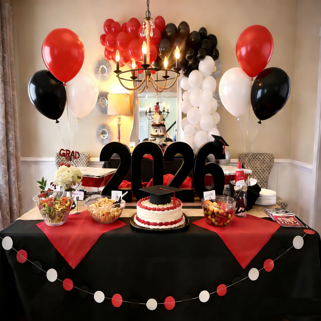 Graduation party table with '2026' numbers, cake, food bowls, and red, black, and white balloons.