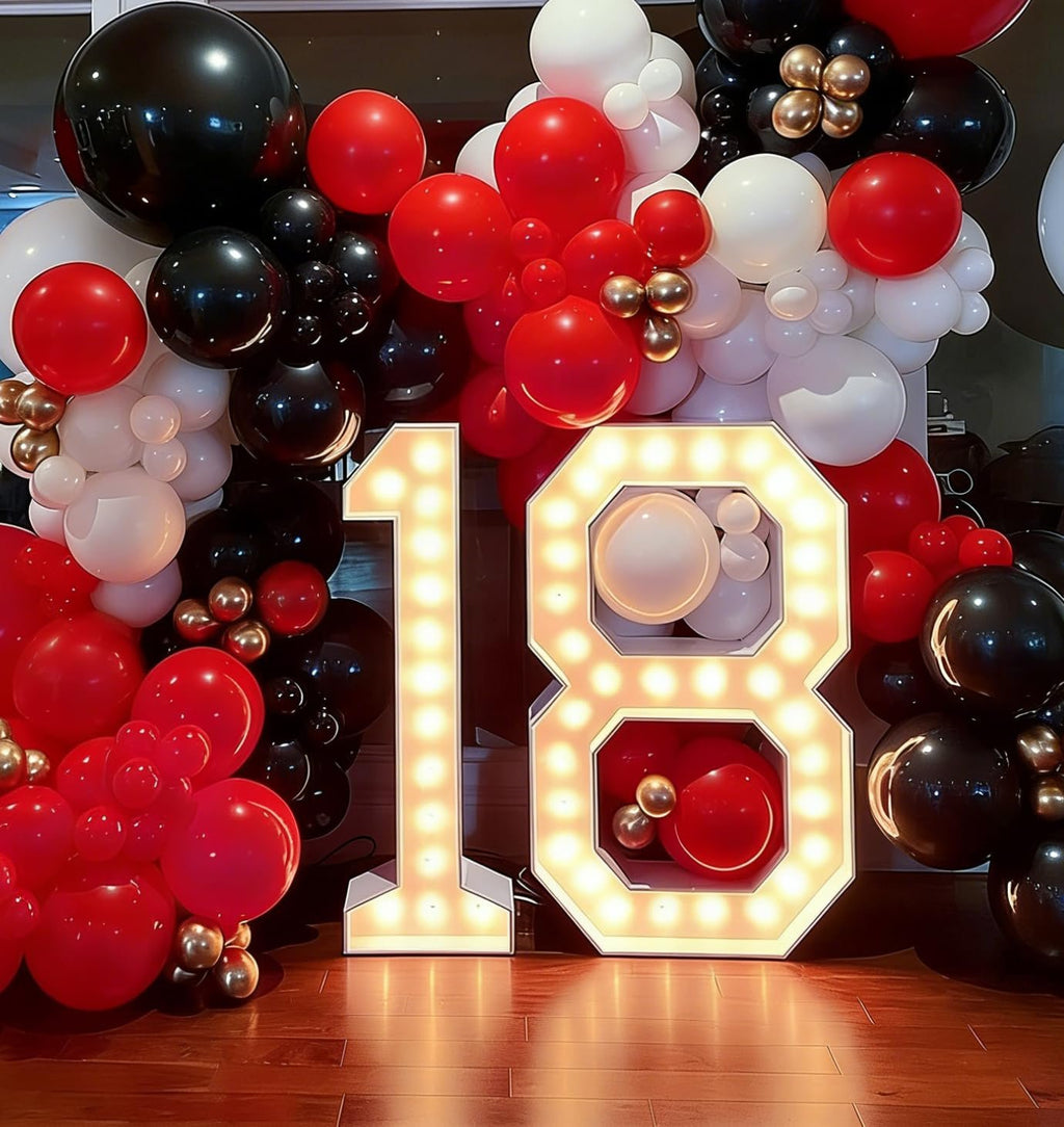 Marquee numbers 18 illuminated with balloons in black, red, white, and gold.