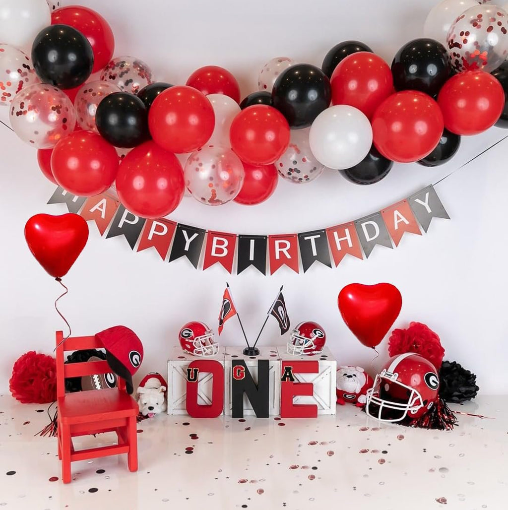 Birthday party setup with balloons, a banner, a red chair, football helmets, and large letters spelling 'ONE'.