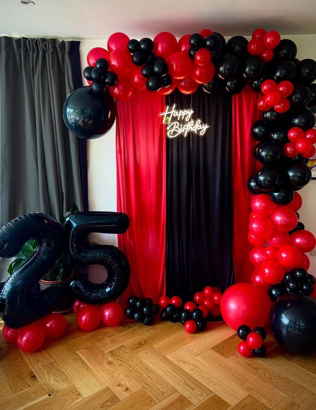 Birthday party decor with black and red balloons forming an arch and a large number 25 balloon.
