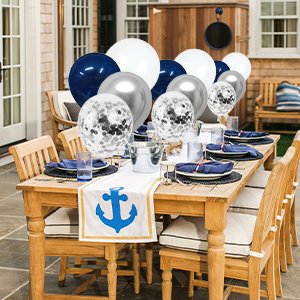 Table setting with navy blue, pearl white, silver, and confetti balloons arranged on a wooden table outdoors.