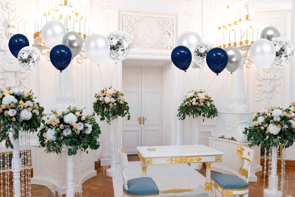Navy blue, pearl white, silver, and confetti balloons float above floral arrangements in a decorated room.