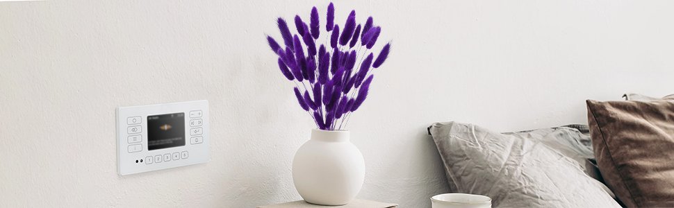 Purple bunny tail grass in a white vase on a shelf next to a white wall panel and pillows