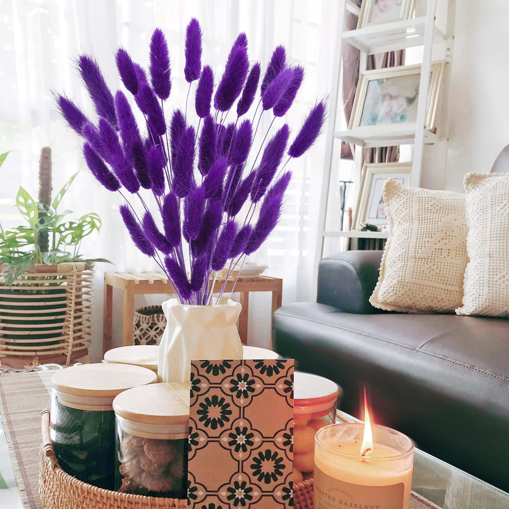Purple bunny tail grass in a vase on a coffee table with decorative jars and a lit candle.