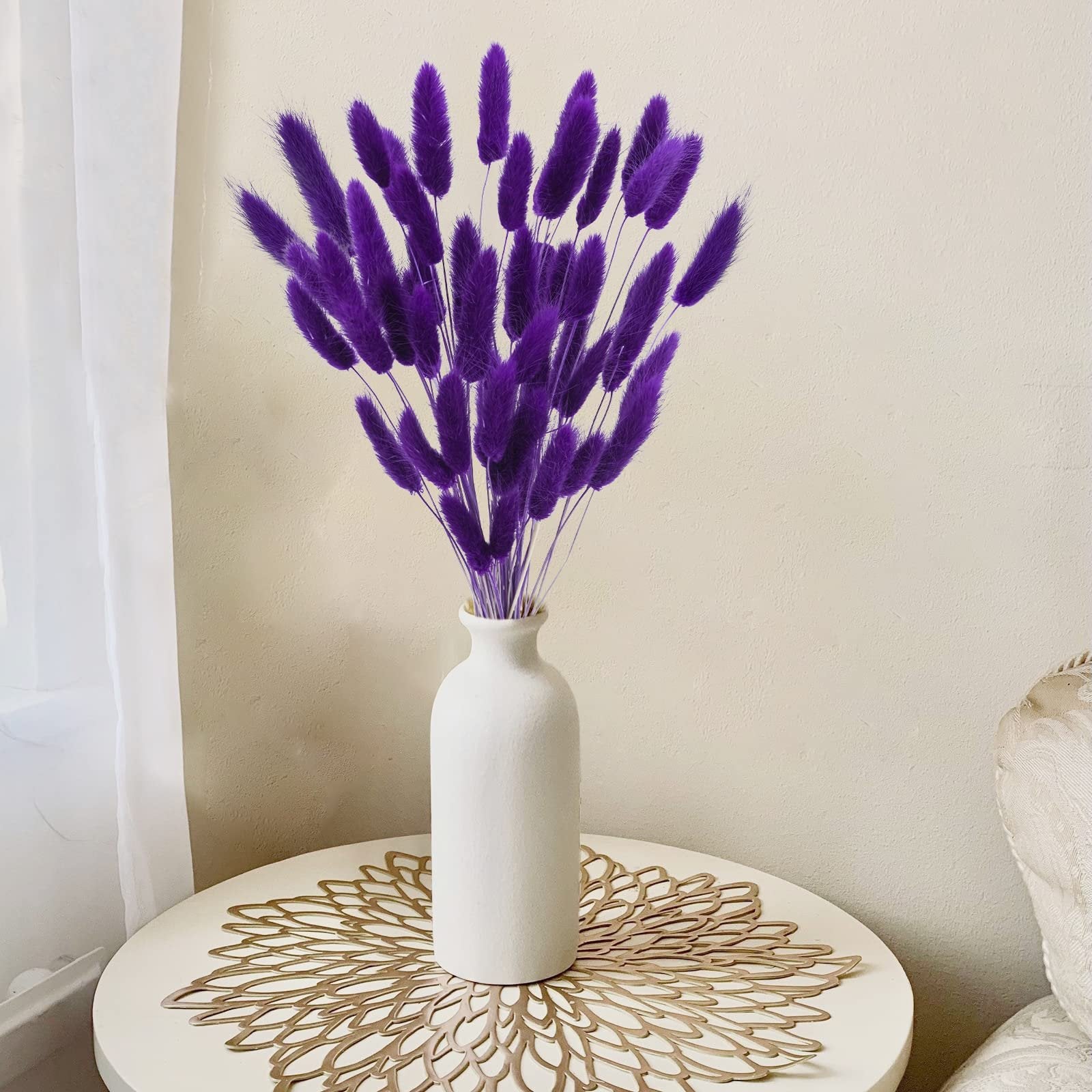 Bunch of purple bunny tail grass stems in a white vase on a round table with a decorative placemat.