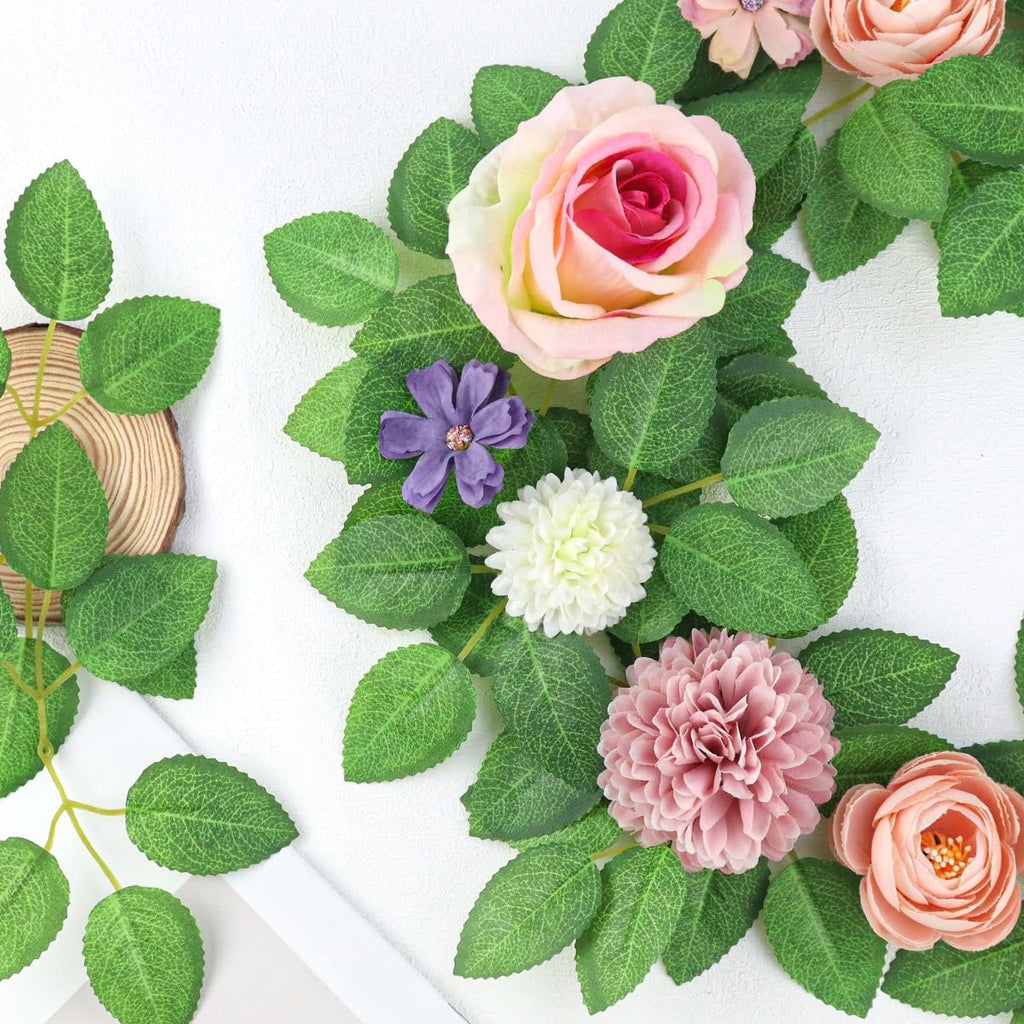 Artificial green rose leaves and assorted silk flowers arranged on a white background with a wood slice.
