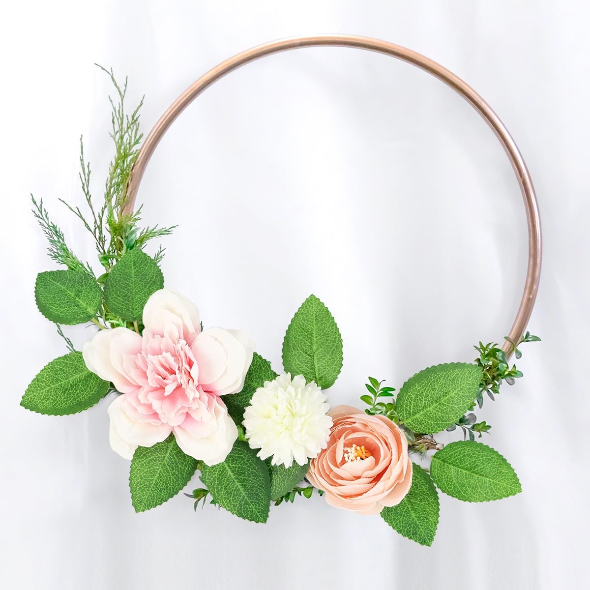 Rose leaves and artificial flowers arranged on a rose gold hoop against a white background