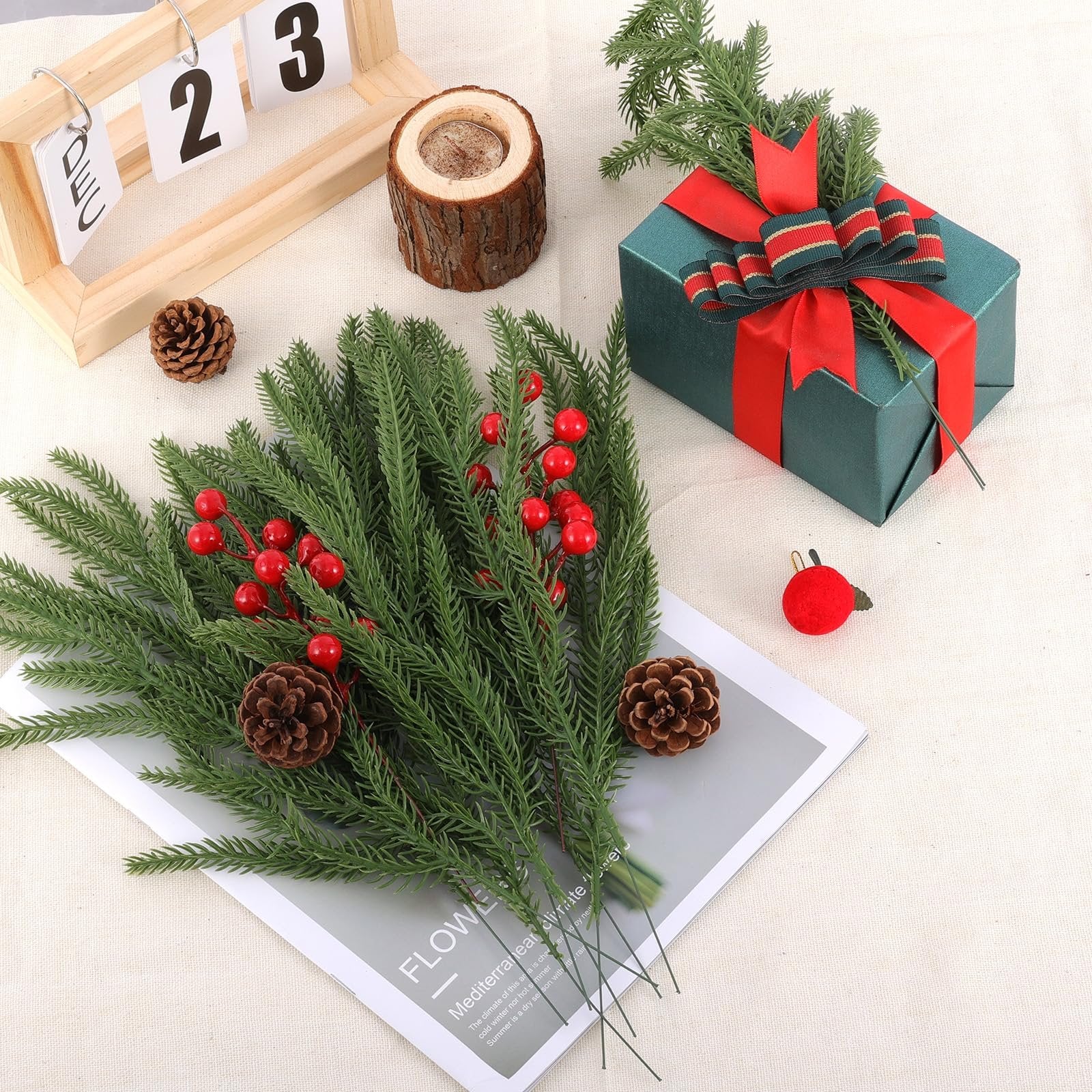 Artificial pine branches with red berries and pine cones arranged with a gift box and wooden calendar