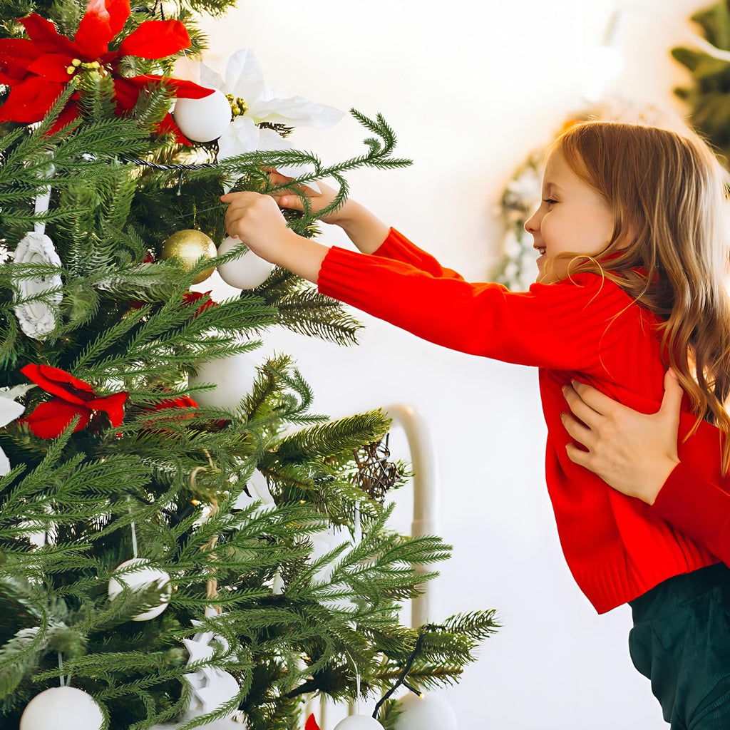 Young girl in red sweater decorating a Christmas tree with ornaments and artificial pine picks.